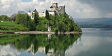 Niedzica Castle reflecting on the serene lake surrounded by lush greenery.