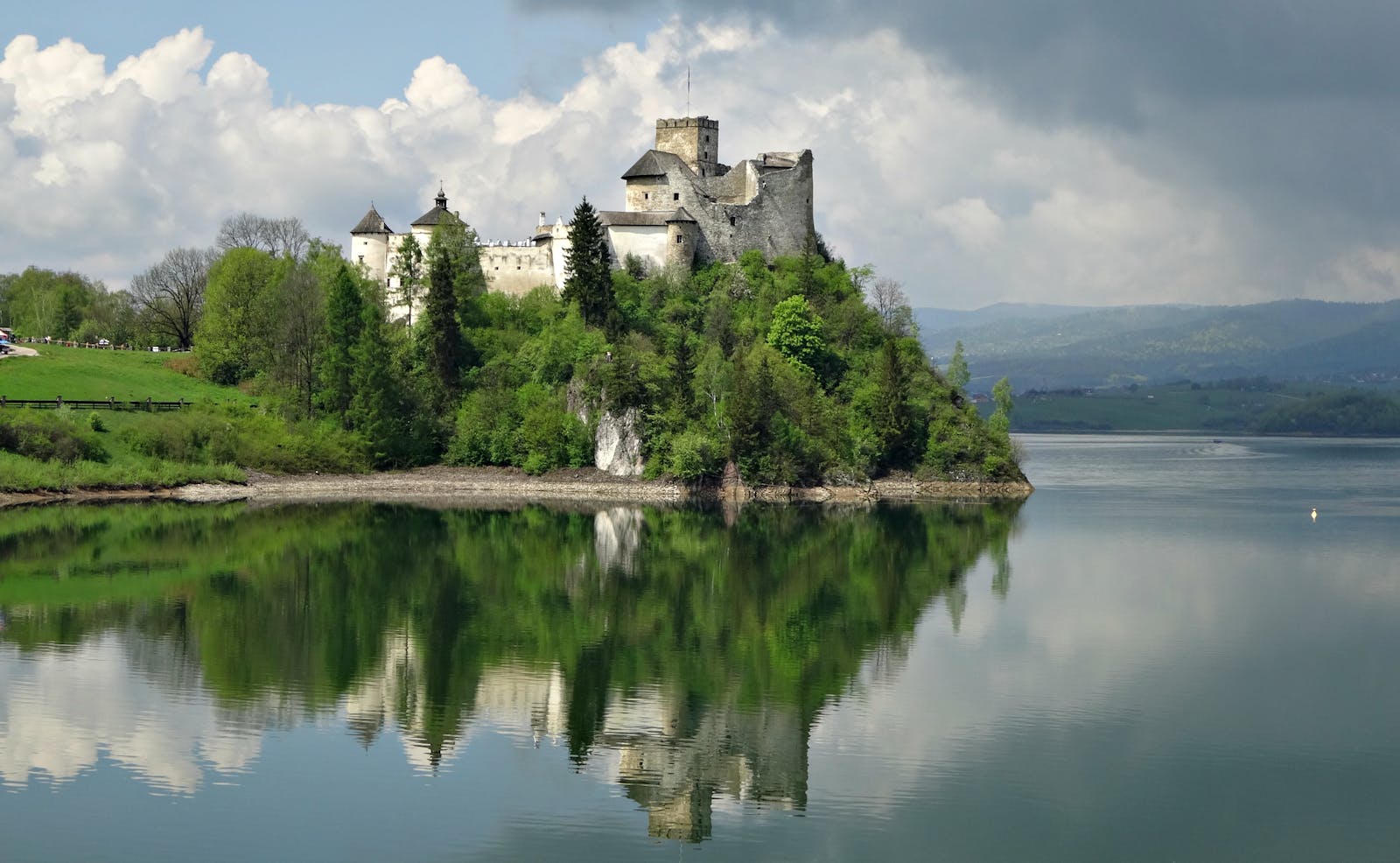 Niedzica Castle reflecting on the serene lake surrounded by lush greenery.